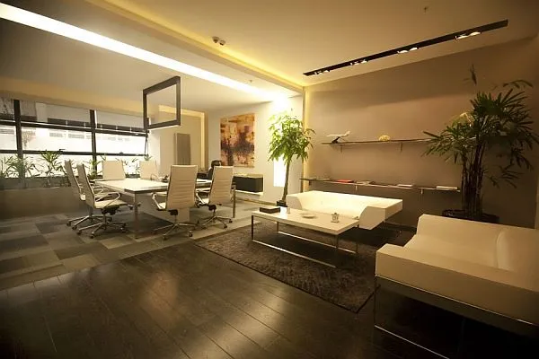 Modern executive office with a conference table, white lounge seating, warm lighting, and indoor plants.